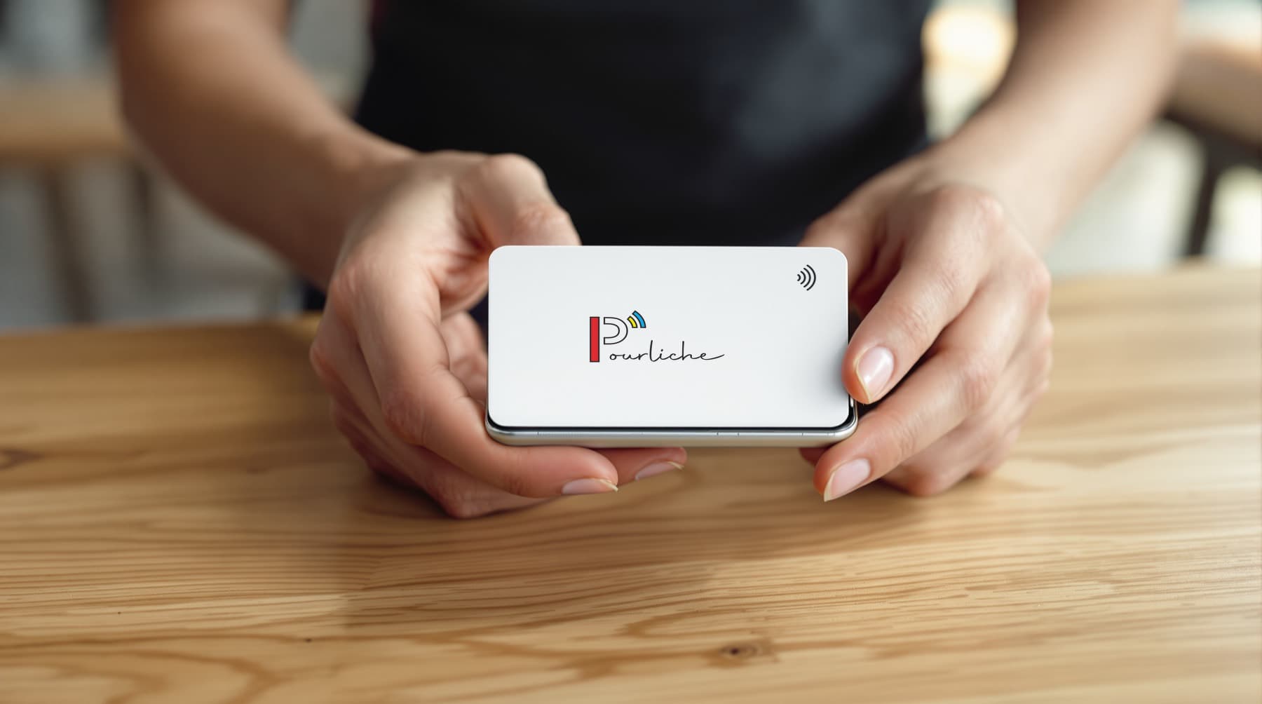 Une carte Pourliche tendue devant un téléphone, au-dessus d’un comptoir en bois